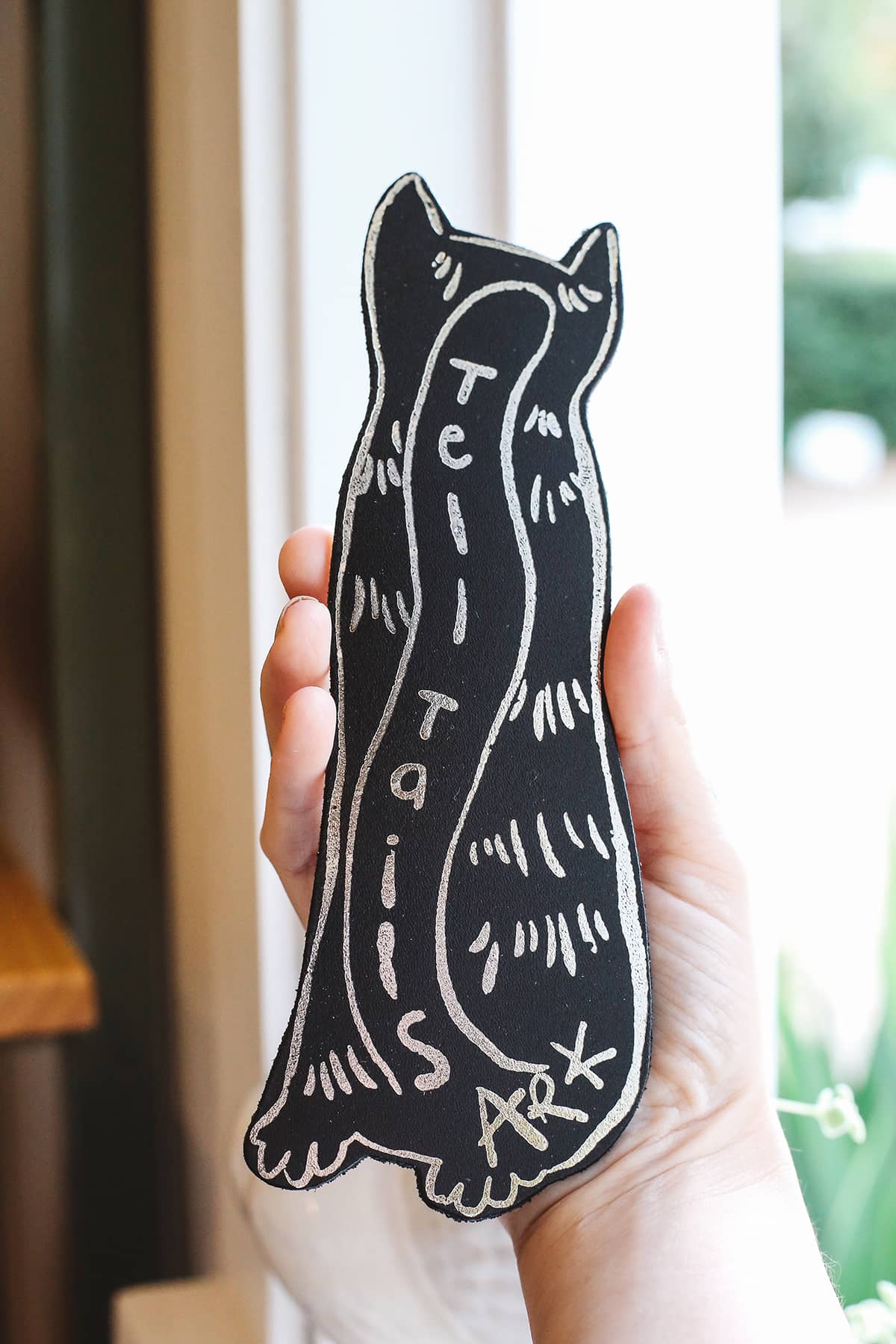 Back of Àine & Co. Ark Bookmark in cat, featuring illustrated black and white cat tail with graphic text "Tell Tails" and ARK signature