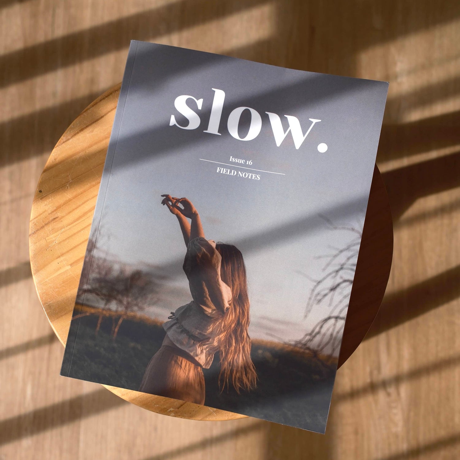 Magazine titled 'slow.' on a wooden surface with a person in a field on the cover.