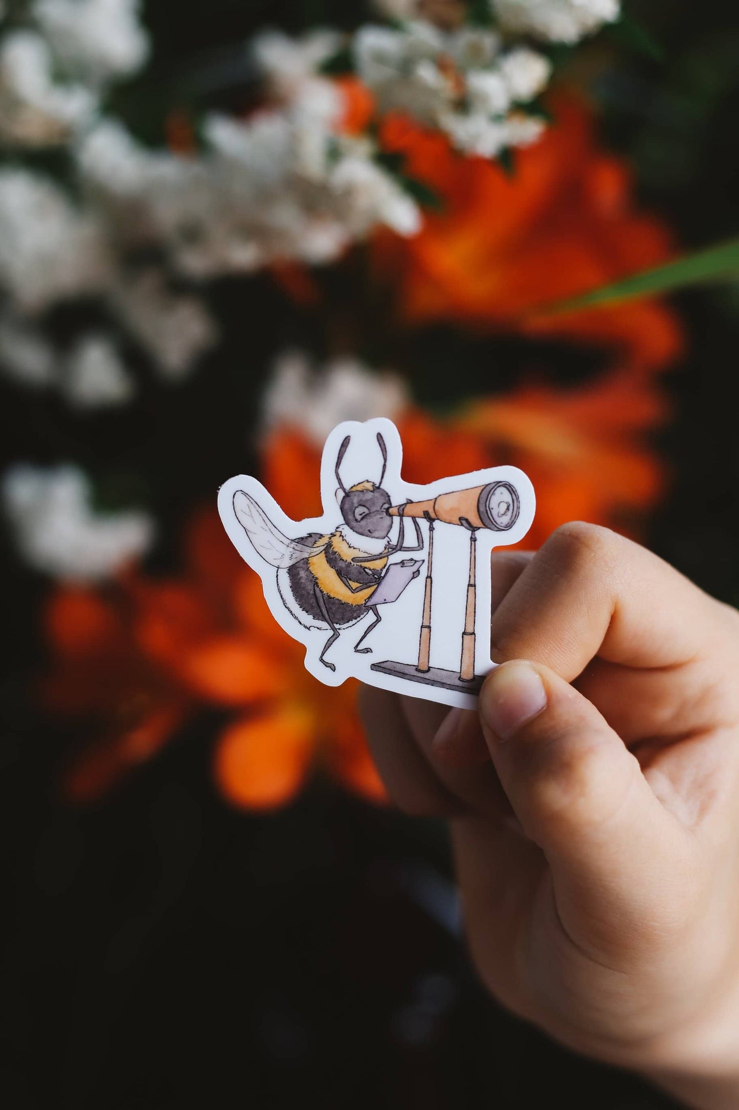 Hand holding a sticker of a bee using a telescope with flowers in the background