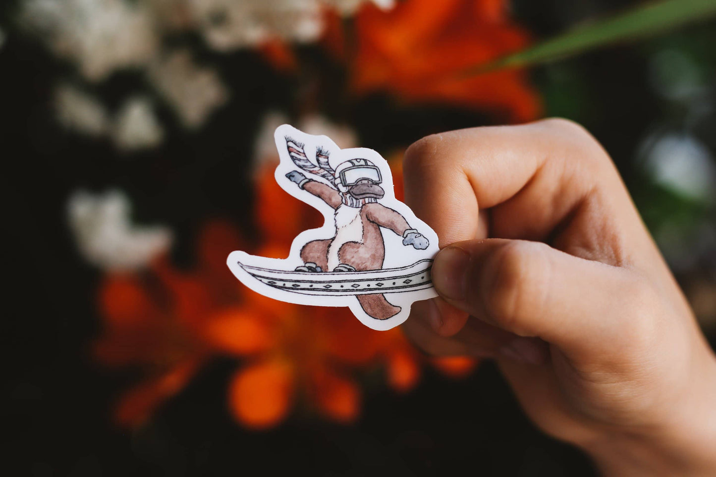 Hand holding a sticker of a platypus skiing