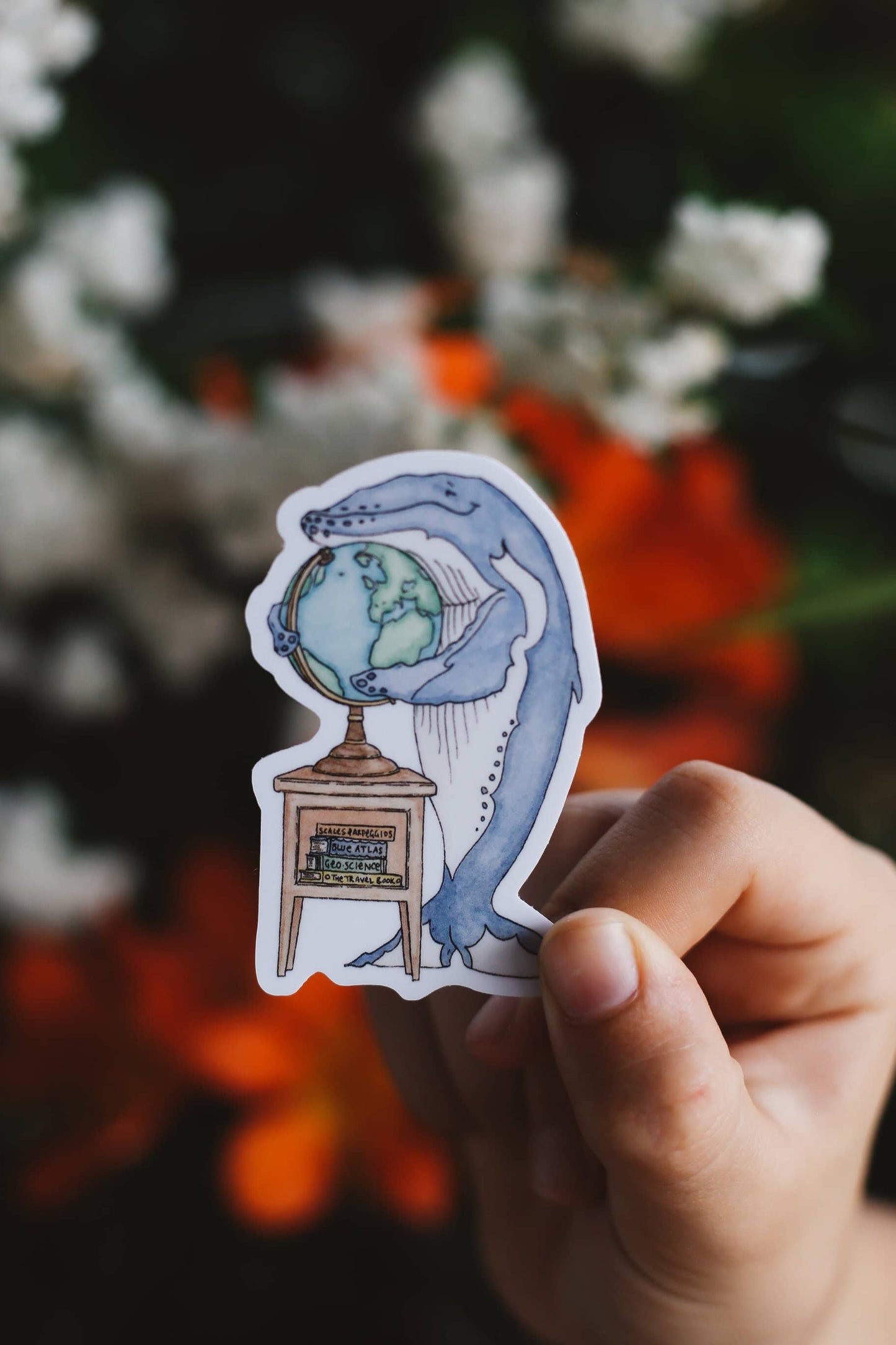 Hand holding a sticker of a whale holding a globe