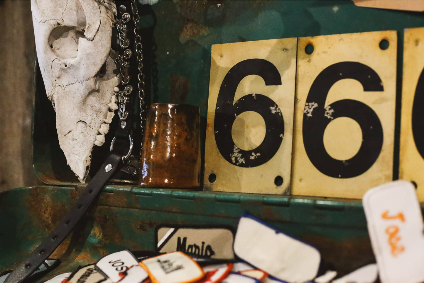 Close-up of a skull, number plates, and Àine & Co. body balm candle on a metal surface.