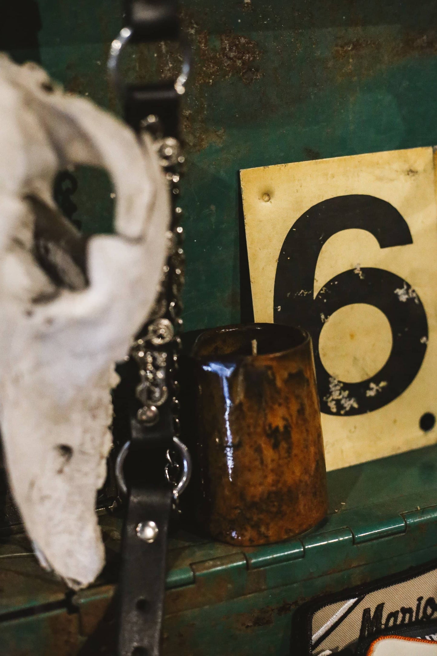 Àine & Co. body balm candle with chain, skull, and number 6 sign on a textured surface