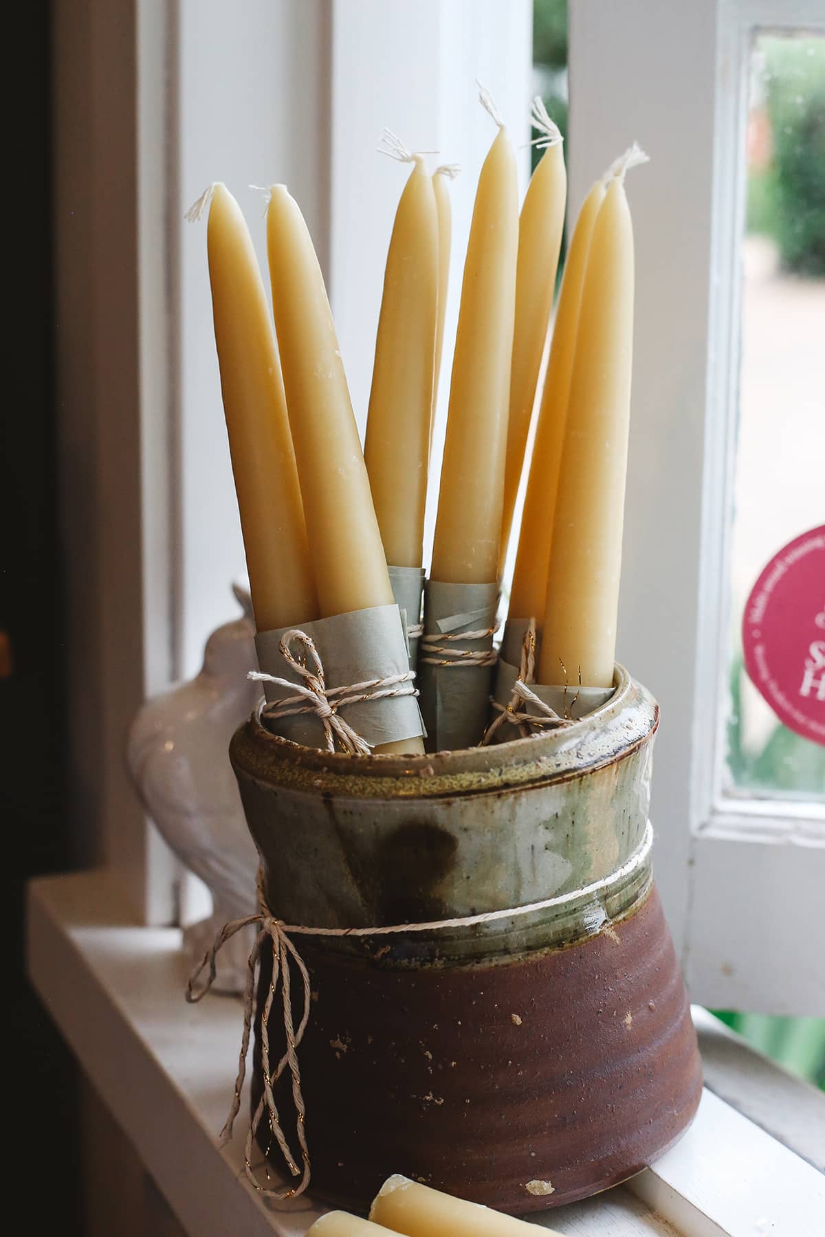 Àine & Co. Bees Wax Candles in "X-Large". Large, tapered, yellow candles with a cotton wick, displayed in a ceramic vessel.