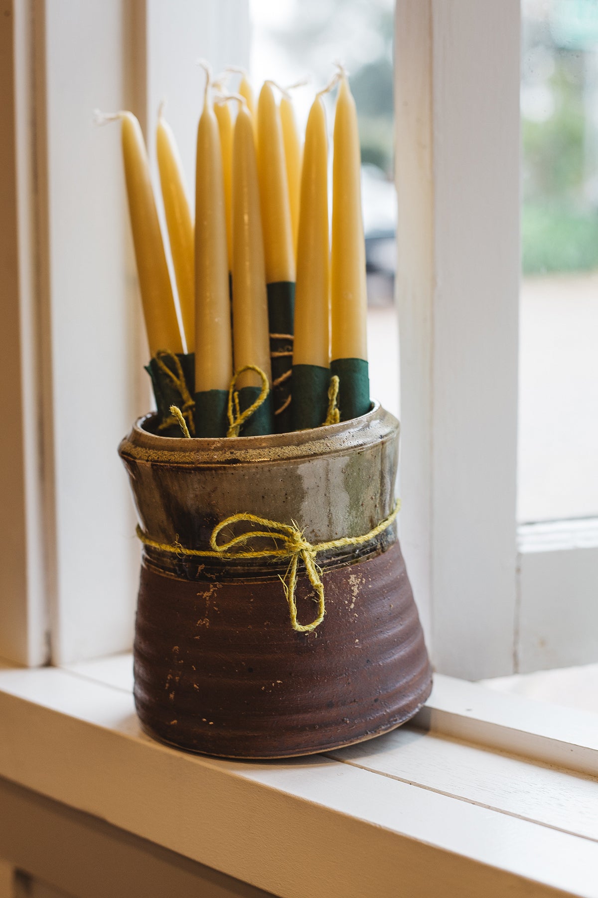 Àine & Co. Bees Wax Candles in "Large". Long, tapered, yellow candles with a cotton wick, displayed in a two-tone ceramic vessel.