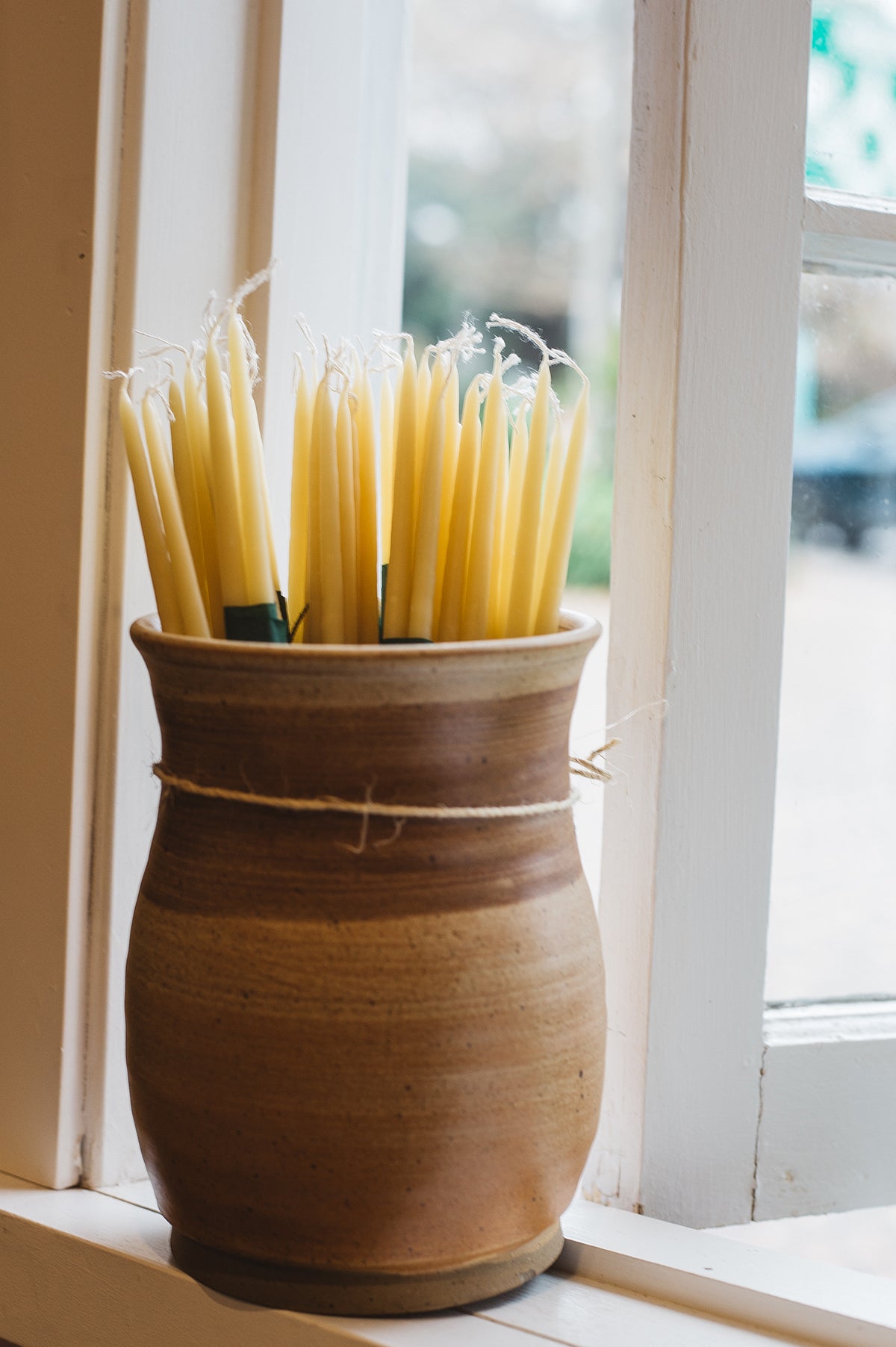 Àine & Co. Bees Wax Candles in "Skinny/Long". Long, thin, tapered, yellow candles with a cotton wick, displayed in a ceramic vessel.