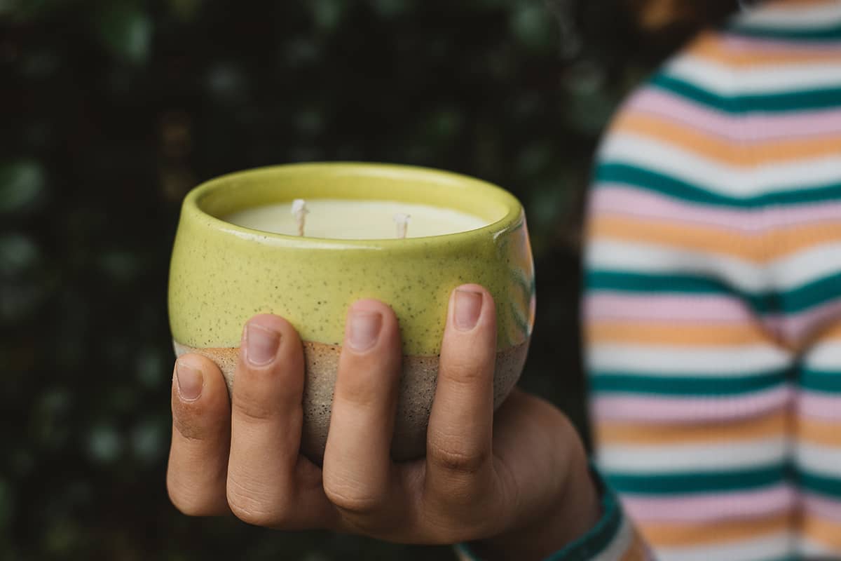 Hand holding Àine & Co. ceramic Comfort Candle Cup in Sásta, featuring a yellow glaze and two cotton wicks.