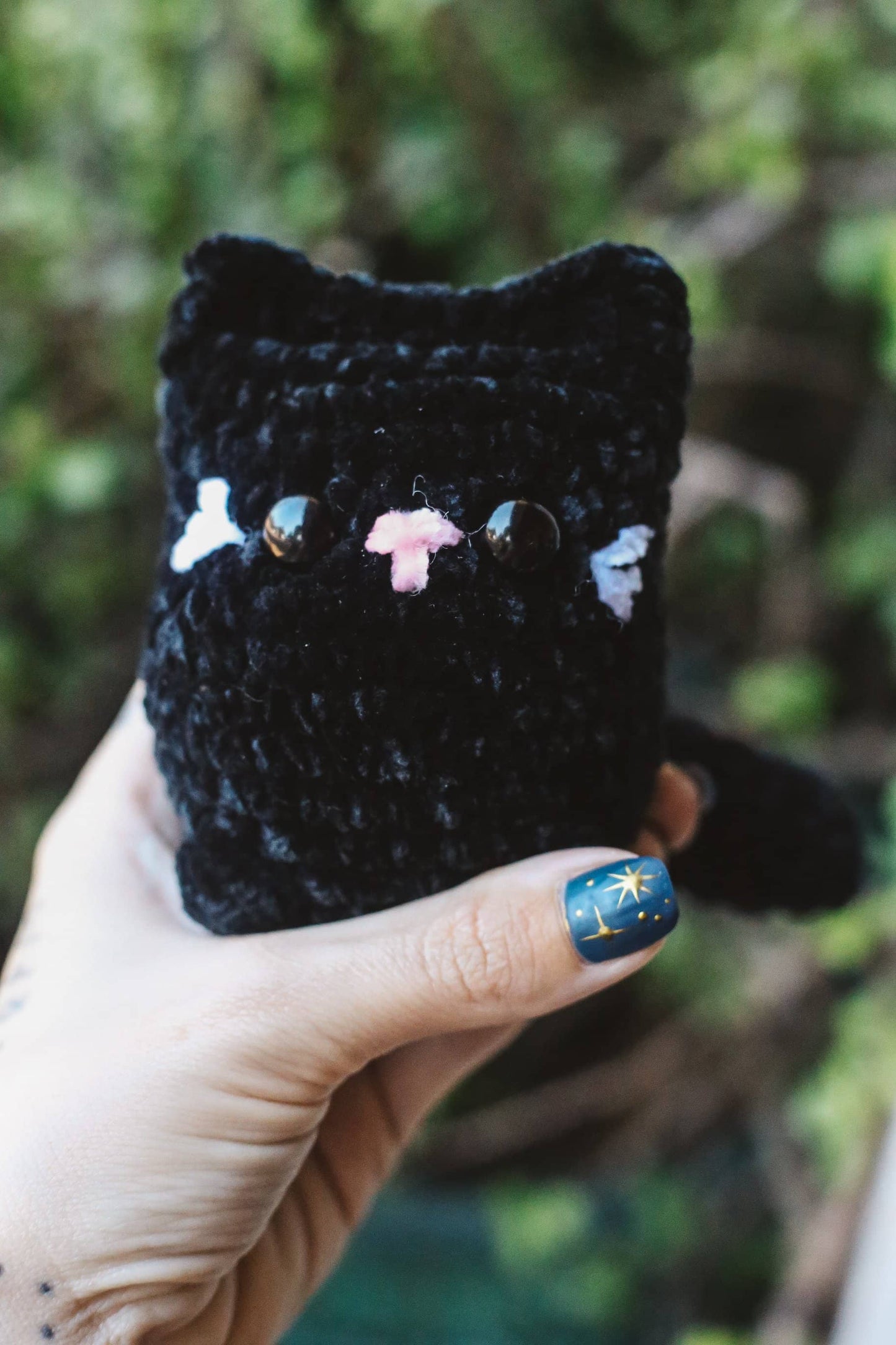 Hand holding a black crochet cat-shaped toy