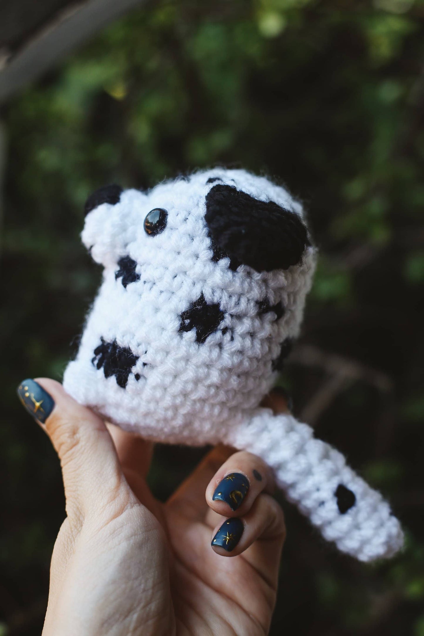 Hand holding a small crochet dalmatian dog toy against a blurred green background