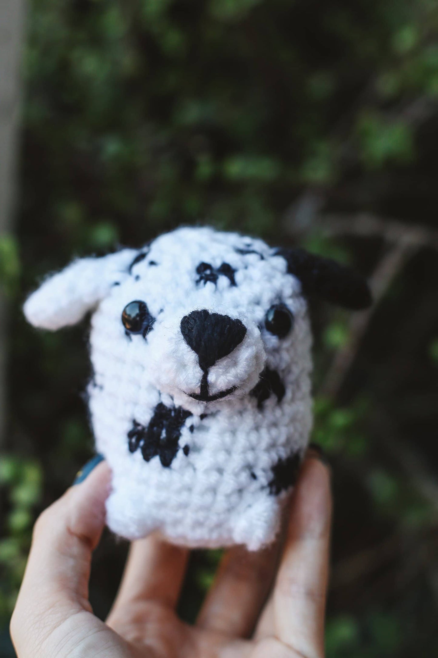 Hand holding a small crochet dalmatian dog toy against a blurred green background