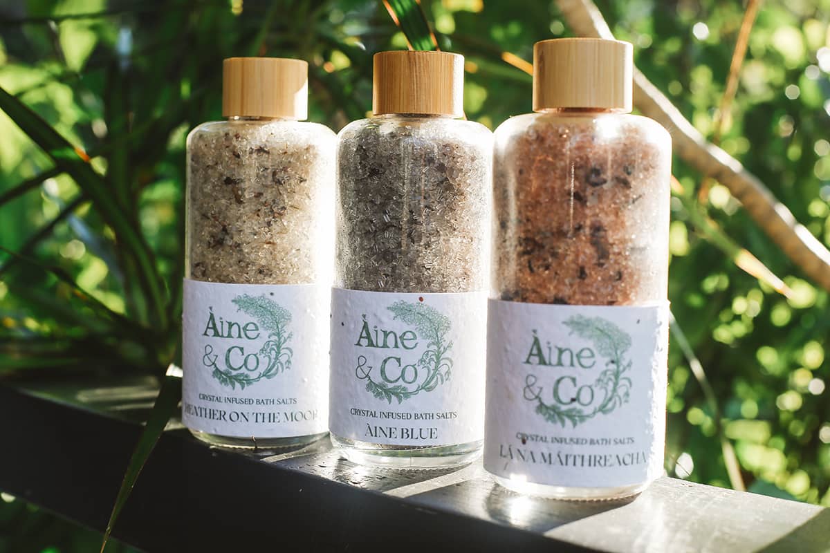 Àine & Co. Crystal Infused Bath Salts in Heather on the Moor, Àine Blue and La Na Maithreacha packaged in glass bottles with wooden lids