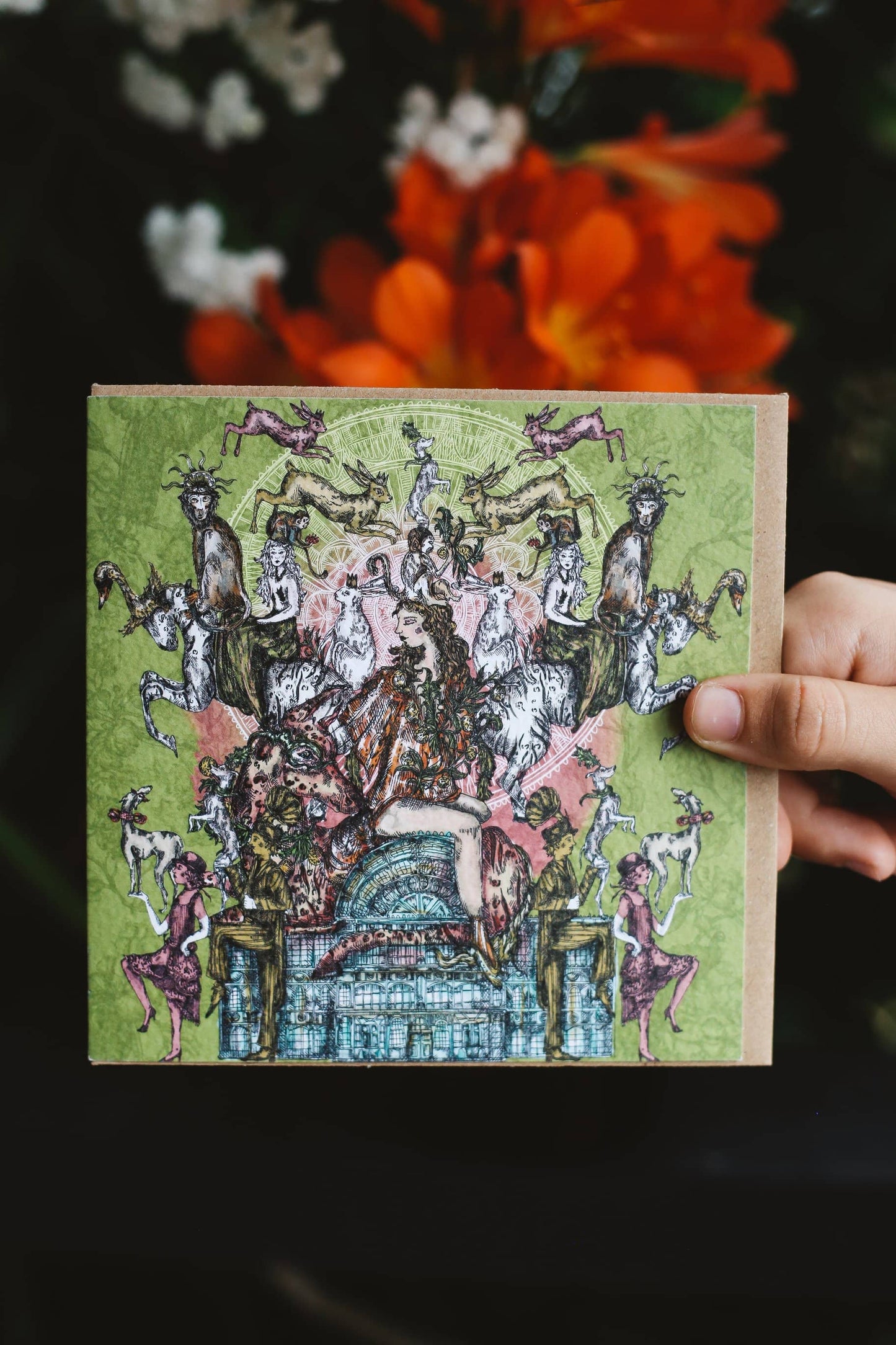 Hand holding a decorative card with intricate illustrations of people and animals on a green background.