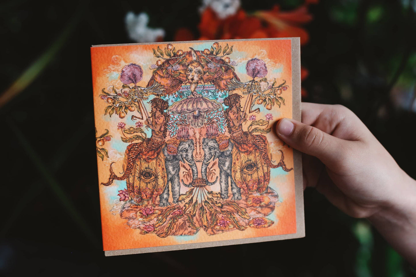 Hand holding a card with intricate design of elephants and floral elements against a dark background