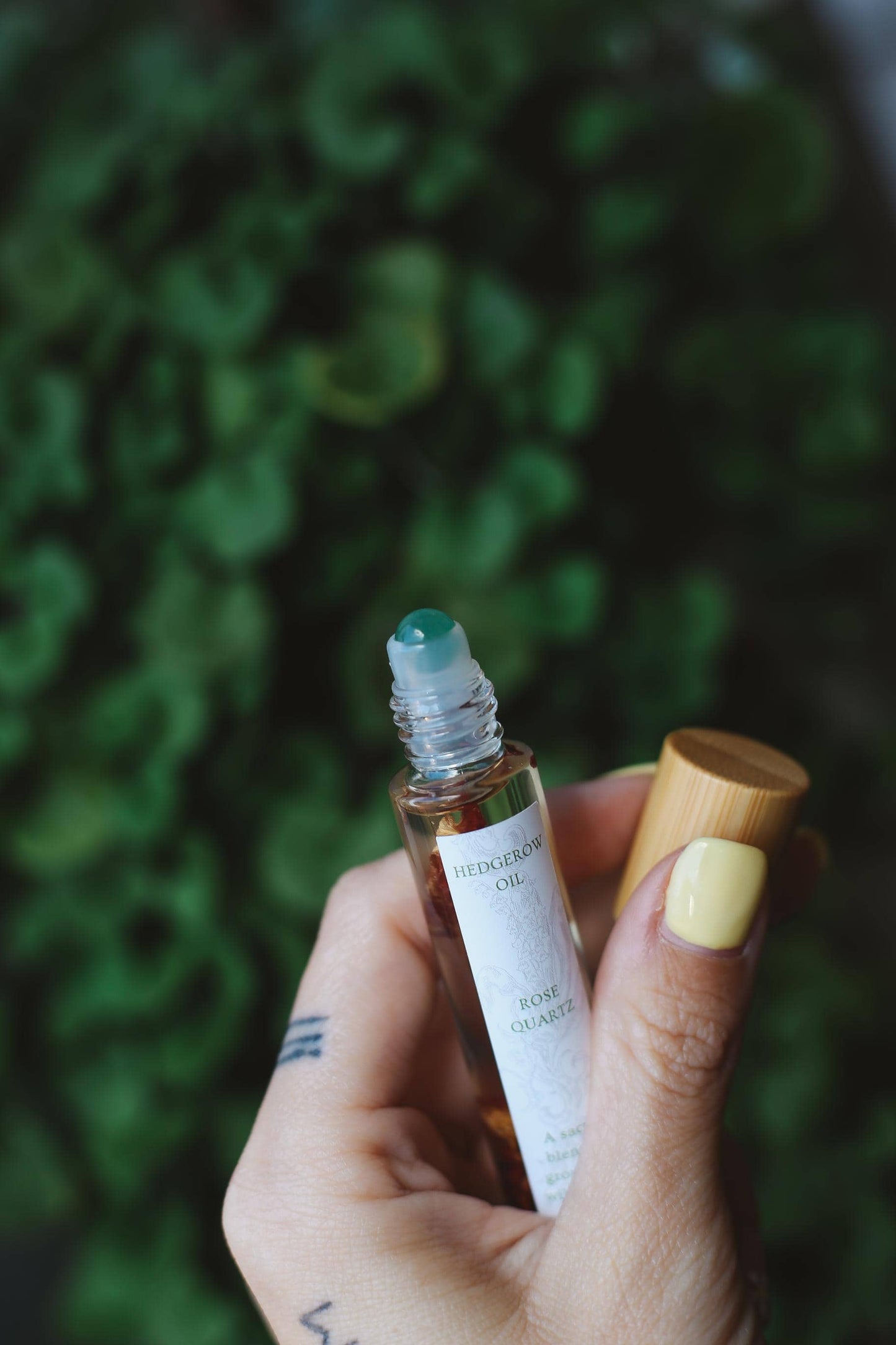 Hand holding a small rollerball bottle with a wooden cap against a blurred green background