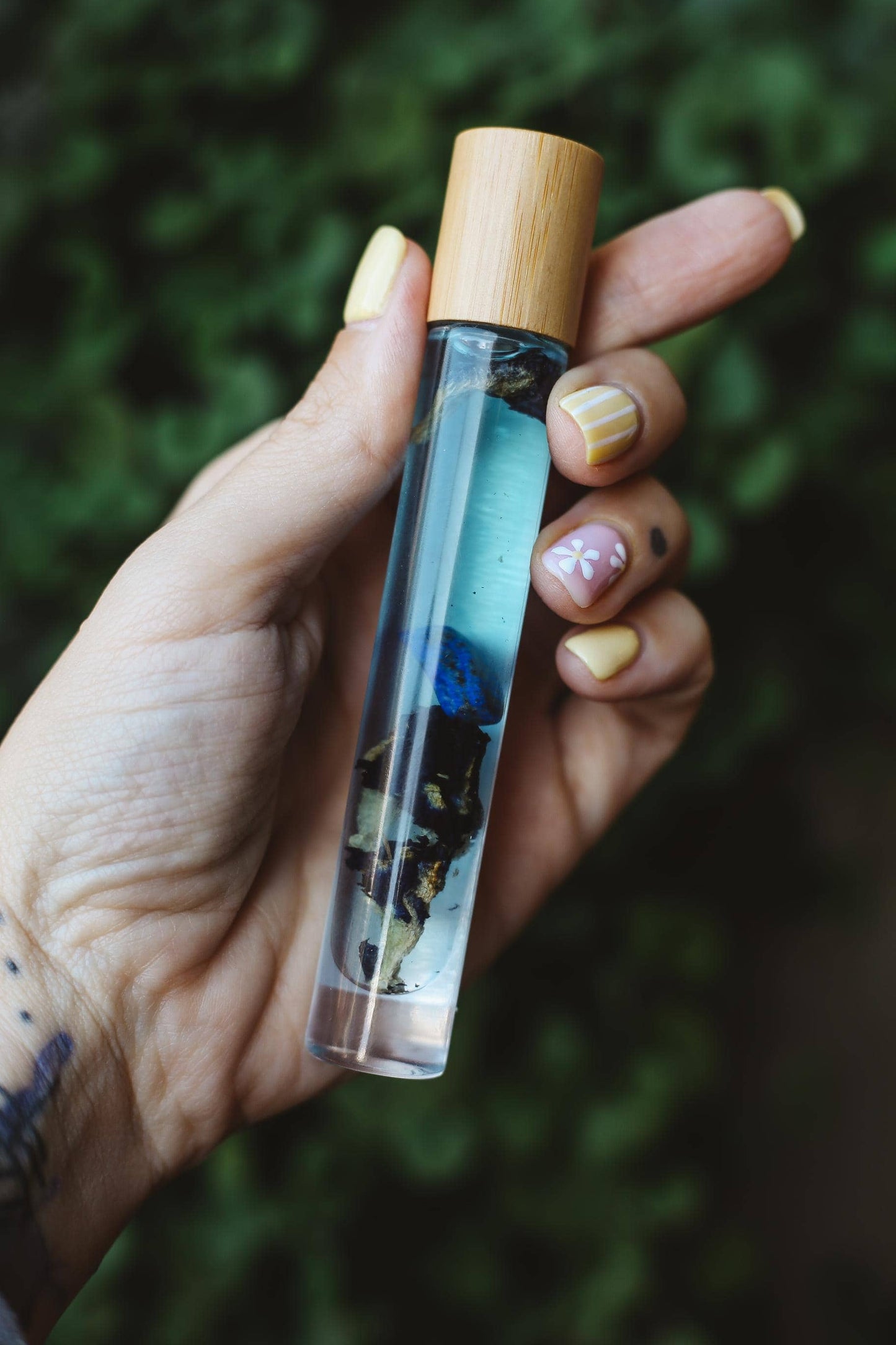 Hand holding a small glass bottle with a wooden cap against a blurred green background