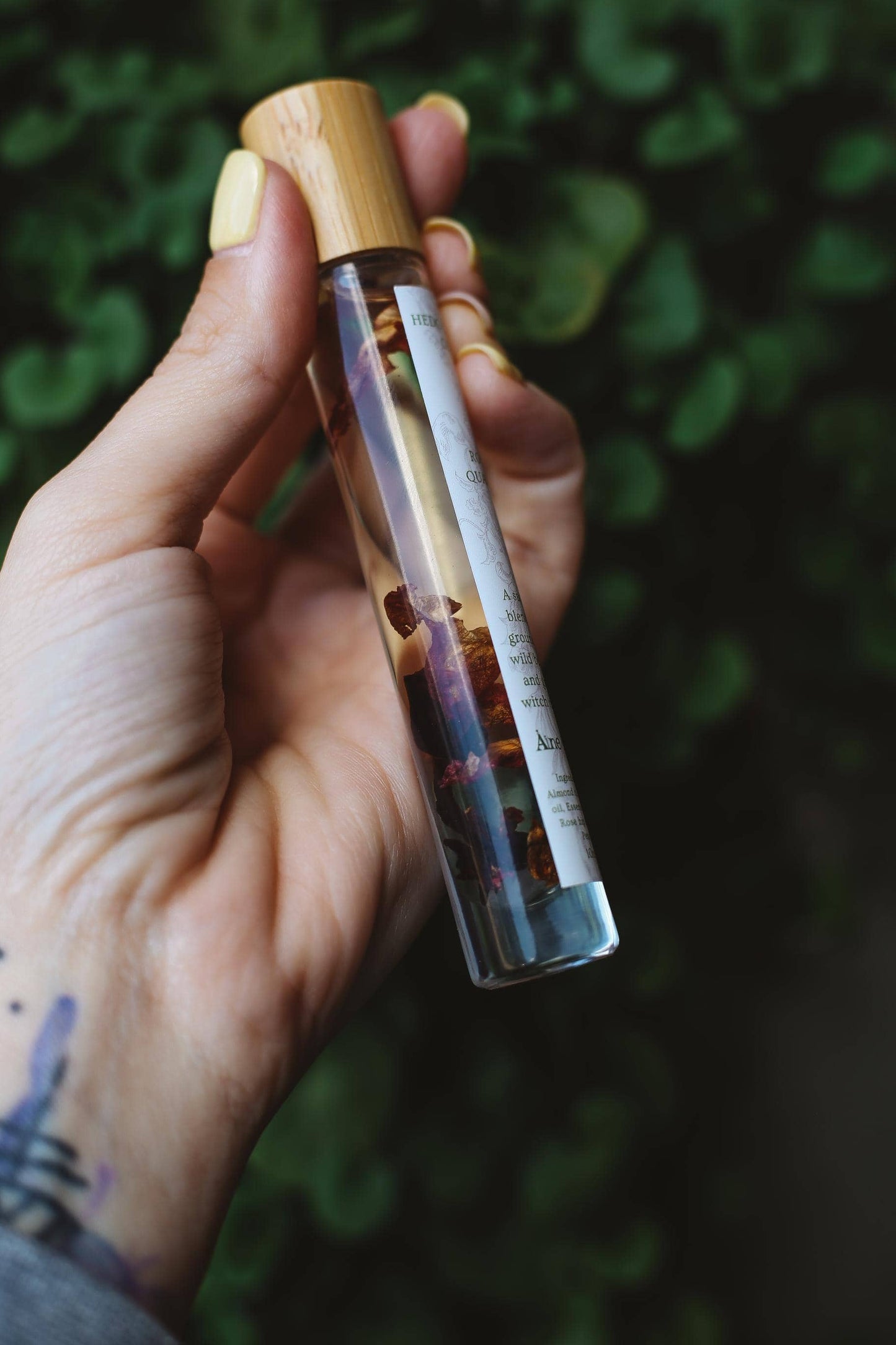 Hand holding a glass vial with a wooden cap against a blurred green background