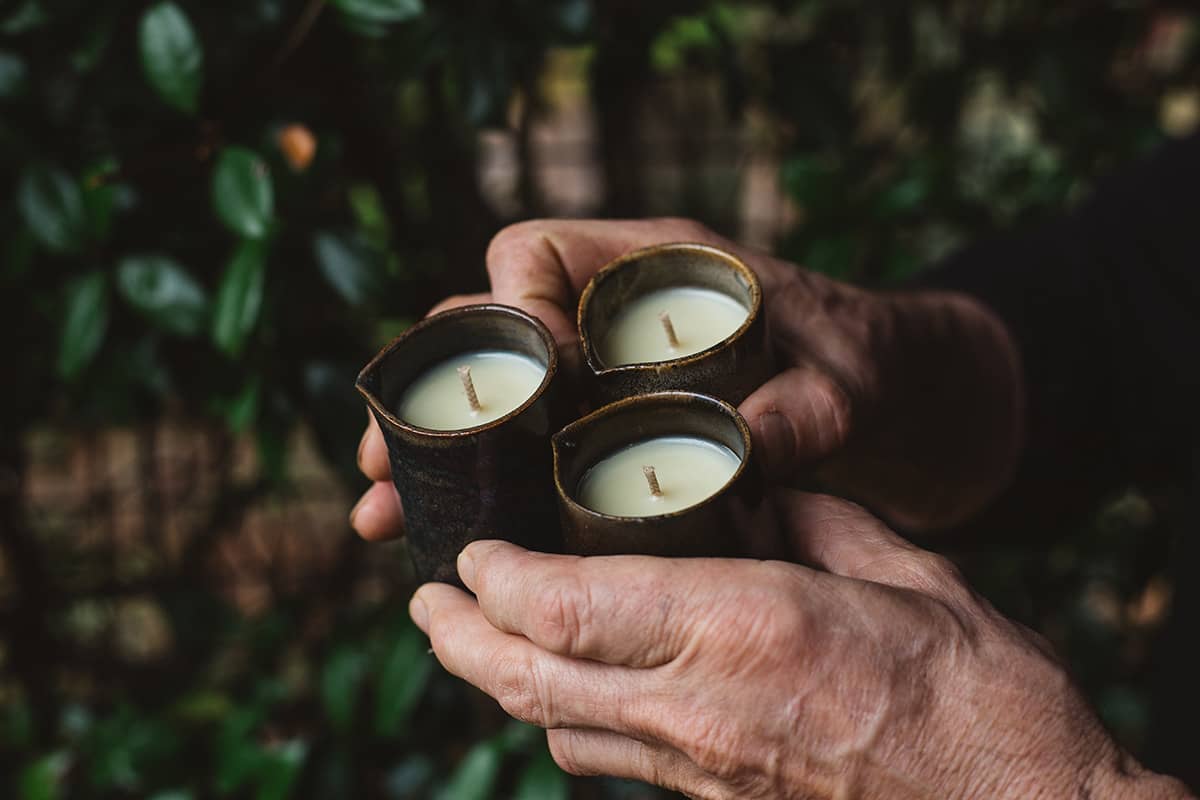 Hands holding three of Àine & Co. Beard and Face Balm Candle with cotton wick in ceramic milk jug