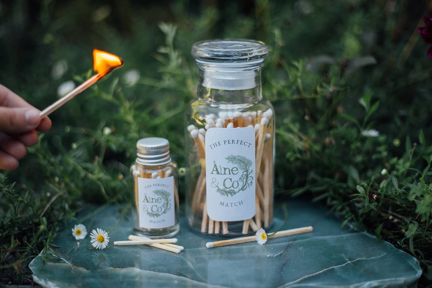 Àine & Co. white matches in glass jars - small and large sizes next to each other with a lit large match
