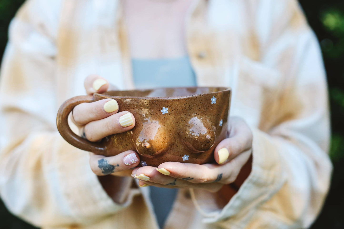 Person holding a brown ceramic cup with daisy pattern outdoors