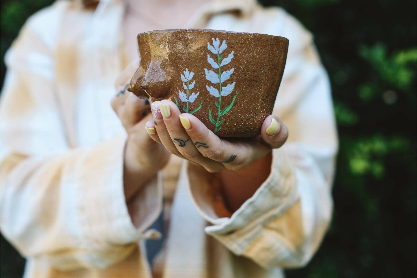 Person holding a ceramic mug with breast shapes and plant designs