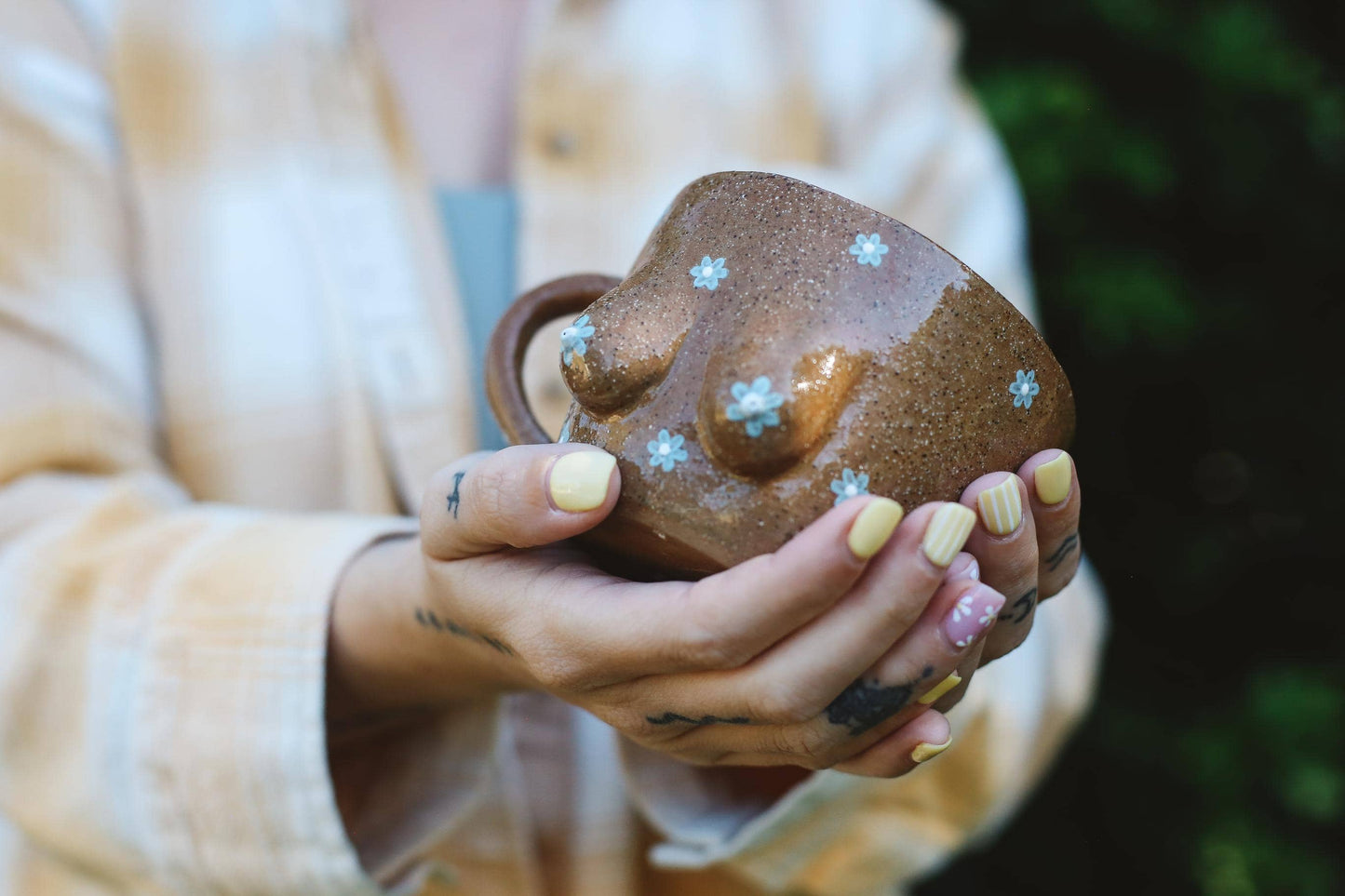 Person holding a ceramic boob design mug with daisy designs.