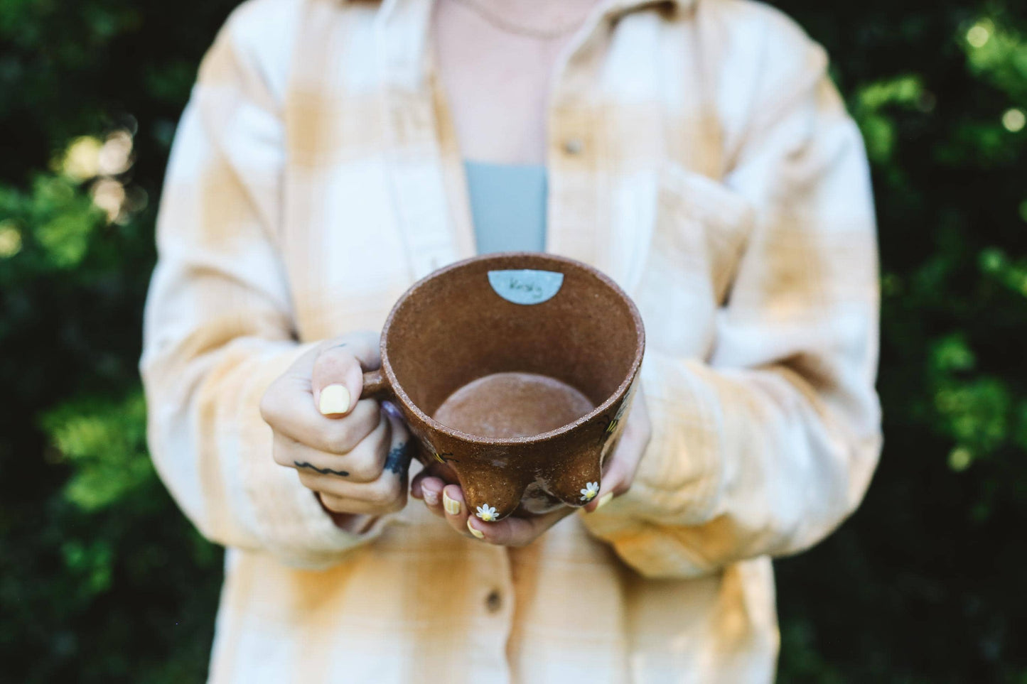 Person holding a brown ceramic cup with a blurred green background