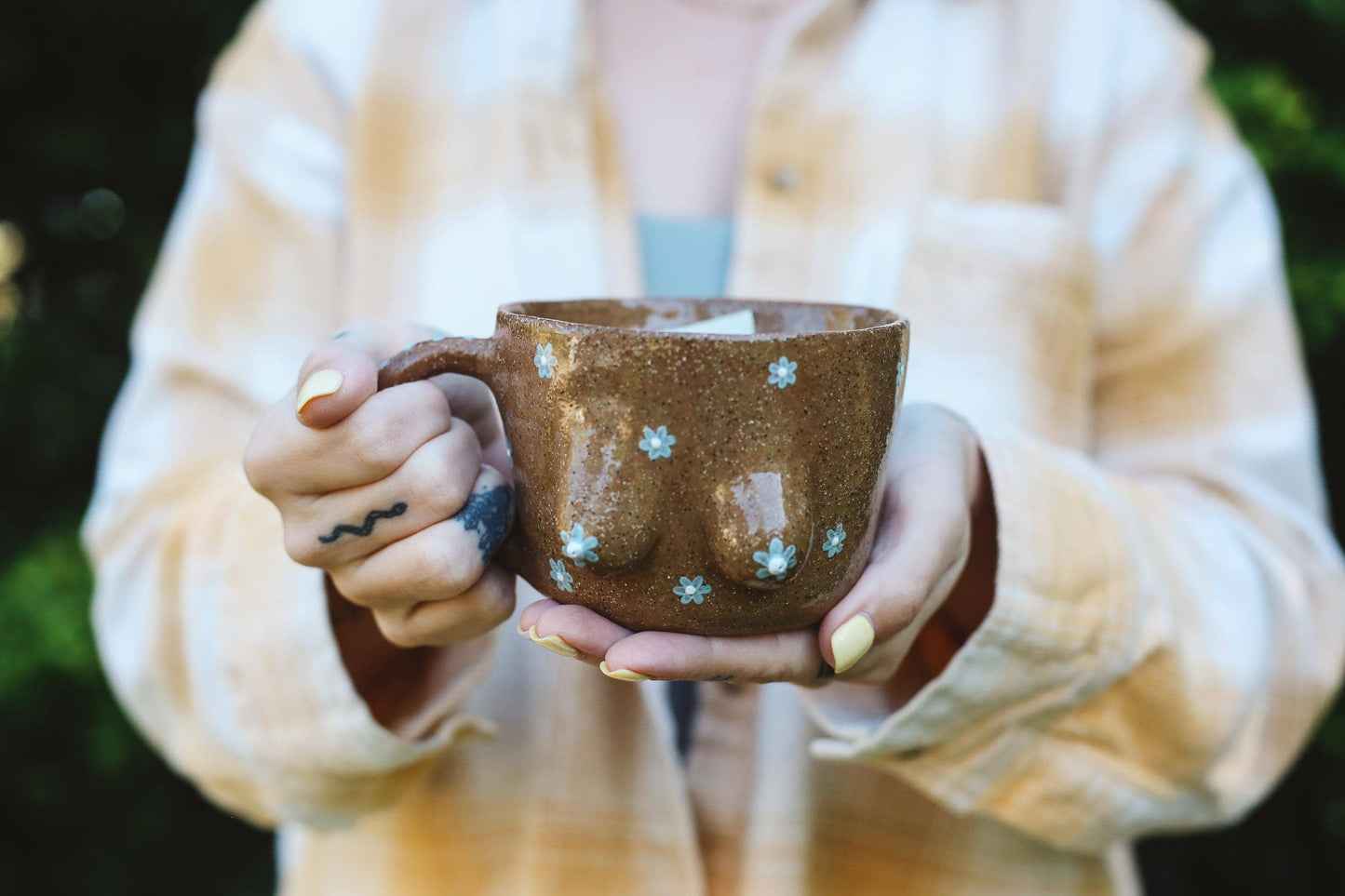 Person holding a brown ceramic mug with painted daisies outdoors
