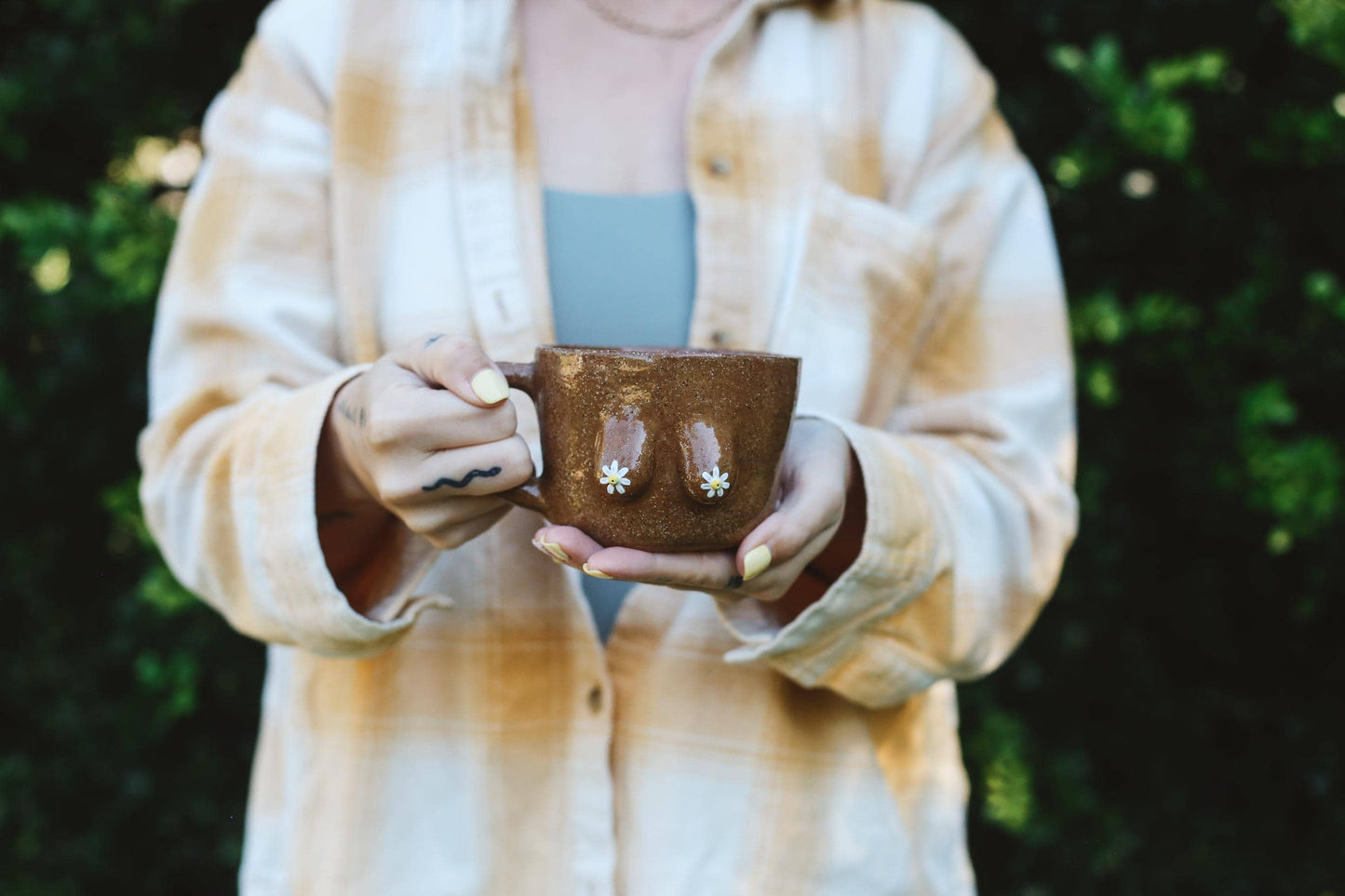 Person holding a brown ceramic cup with a blurred background