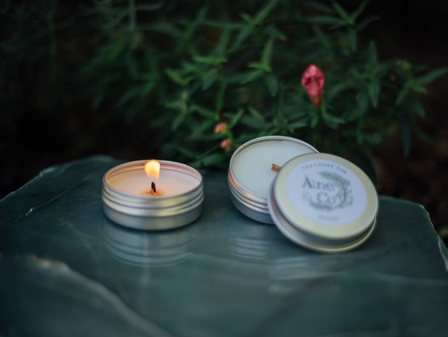 Àine & Co. Tea Light Tins lit with a wooden wick, next to an unlit Tea Light Tin