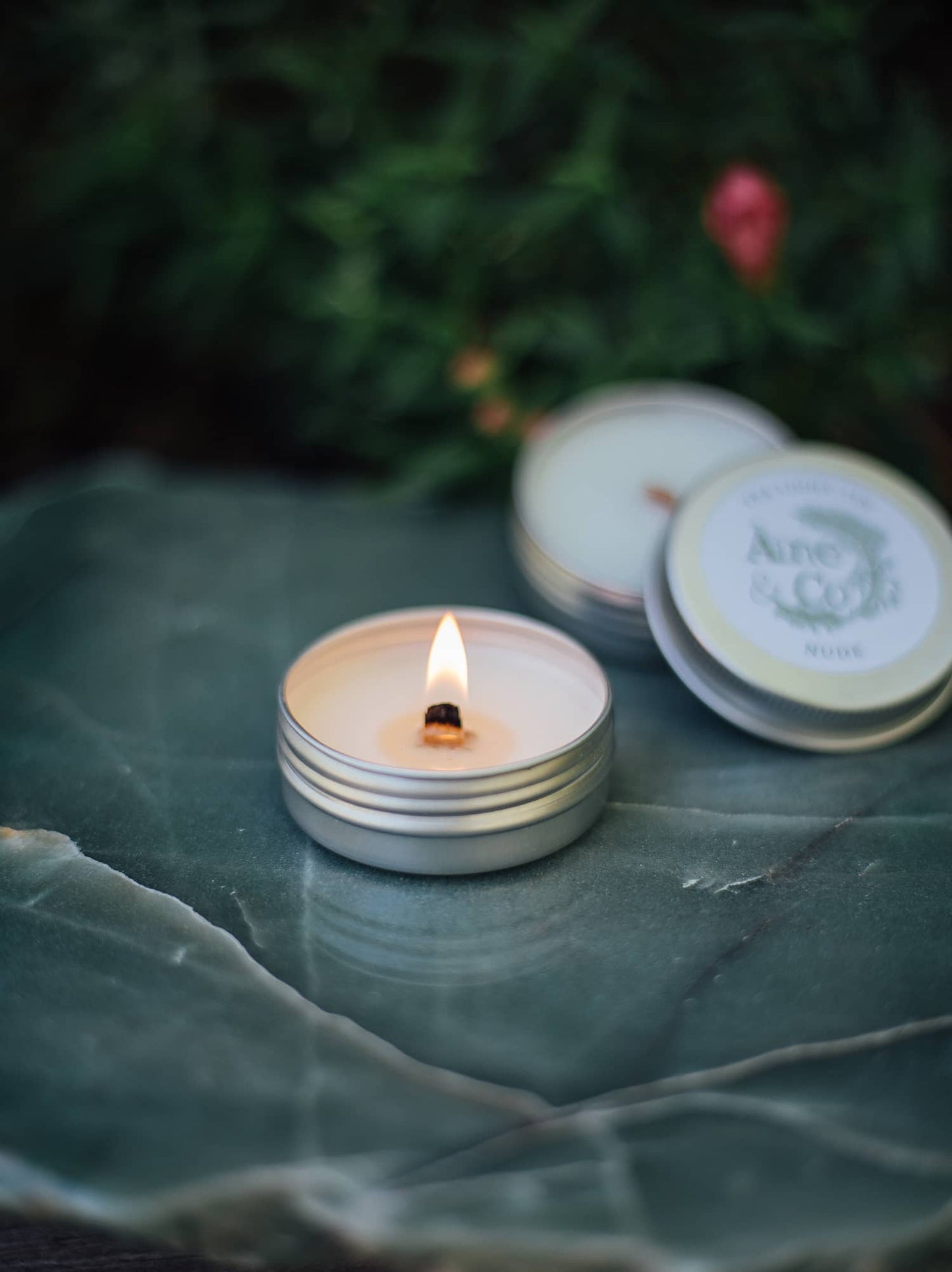 Àine & Co. Tea Light Tins lit with a wooden wick, next to an unlit Tea Light Tin