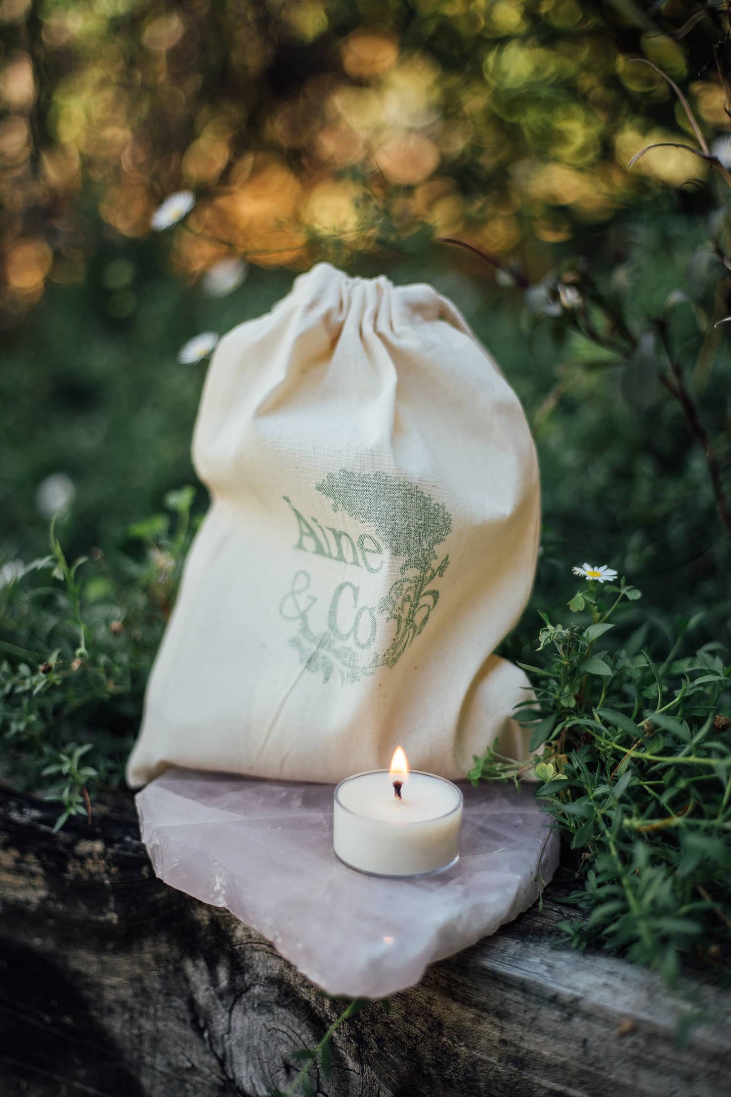 A lit Àine & Co. Tea Light in size small, shown with the Àine & Co. logo calico drawstring bag
