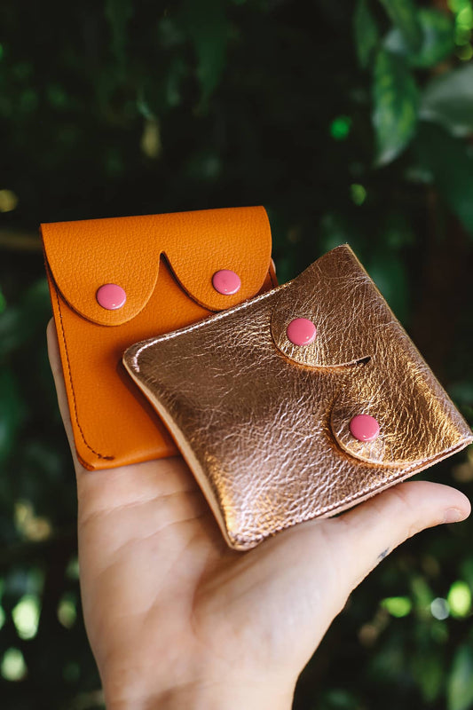 Hand holding Àine & Co. Alkemest Boobie Coin Purses in Gold and Orange (Tan)