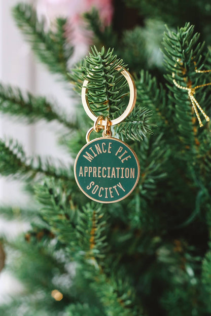 Àine & Co. Alphabet Bags metal keyring featuring circle shape with gold hardware and gold text "Mince Pie Appreciation Society" on dark green background