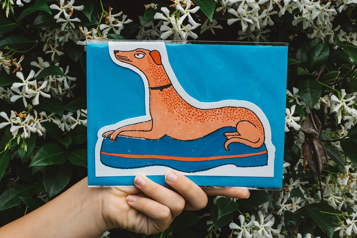 Àine & Co. Archivist greeting card featuring greyhound laying on blue bed