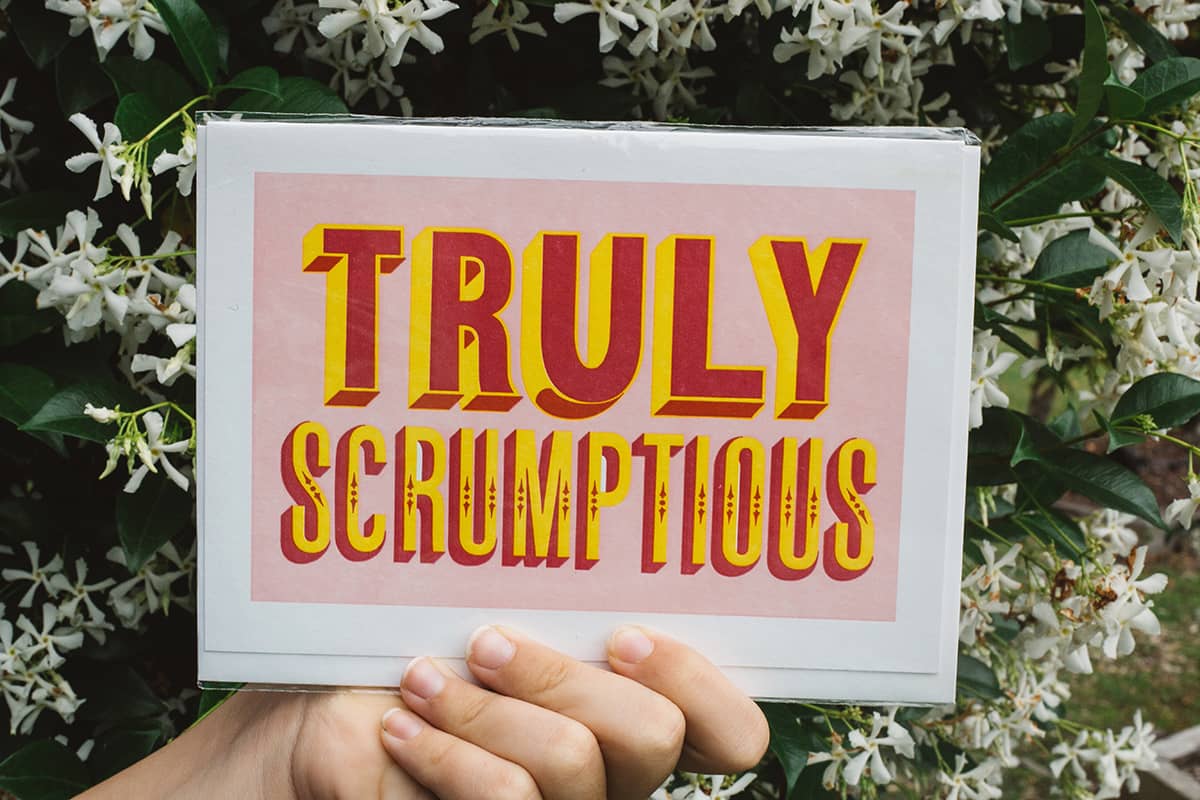Àine & Co. Archivist greeting card featuring bold red and yellow text "Truly Scrumptious" on pastel pink background