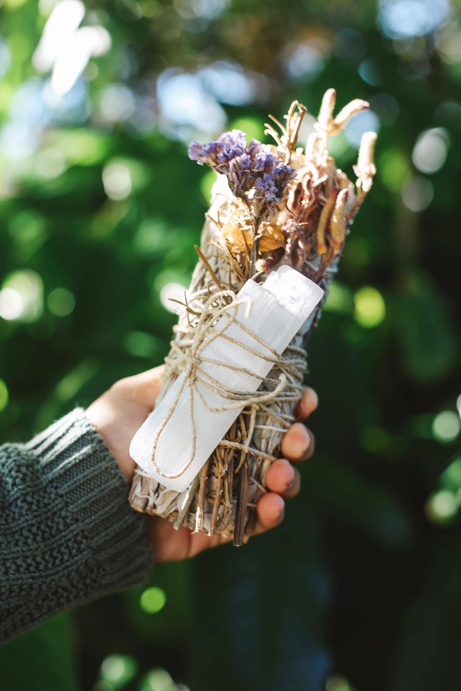 Hand holding a bundle of sage and lavender with a blurred green background