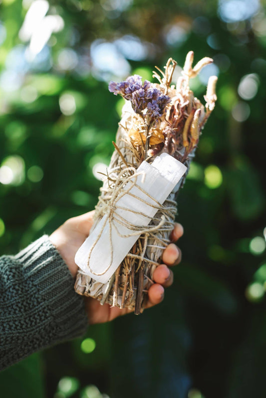 Hand holding a bundle of sage and lavender with a blurred green background
