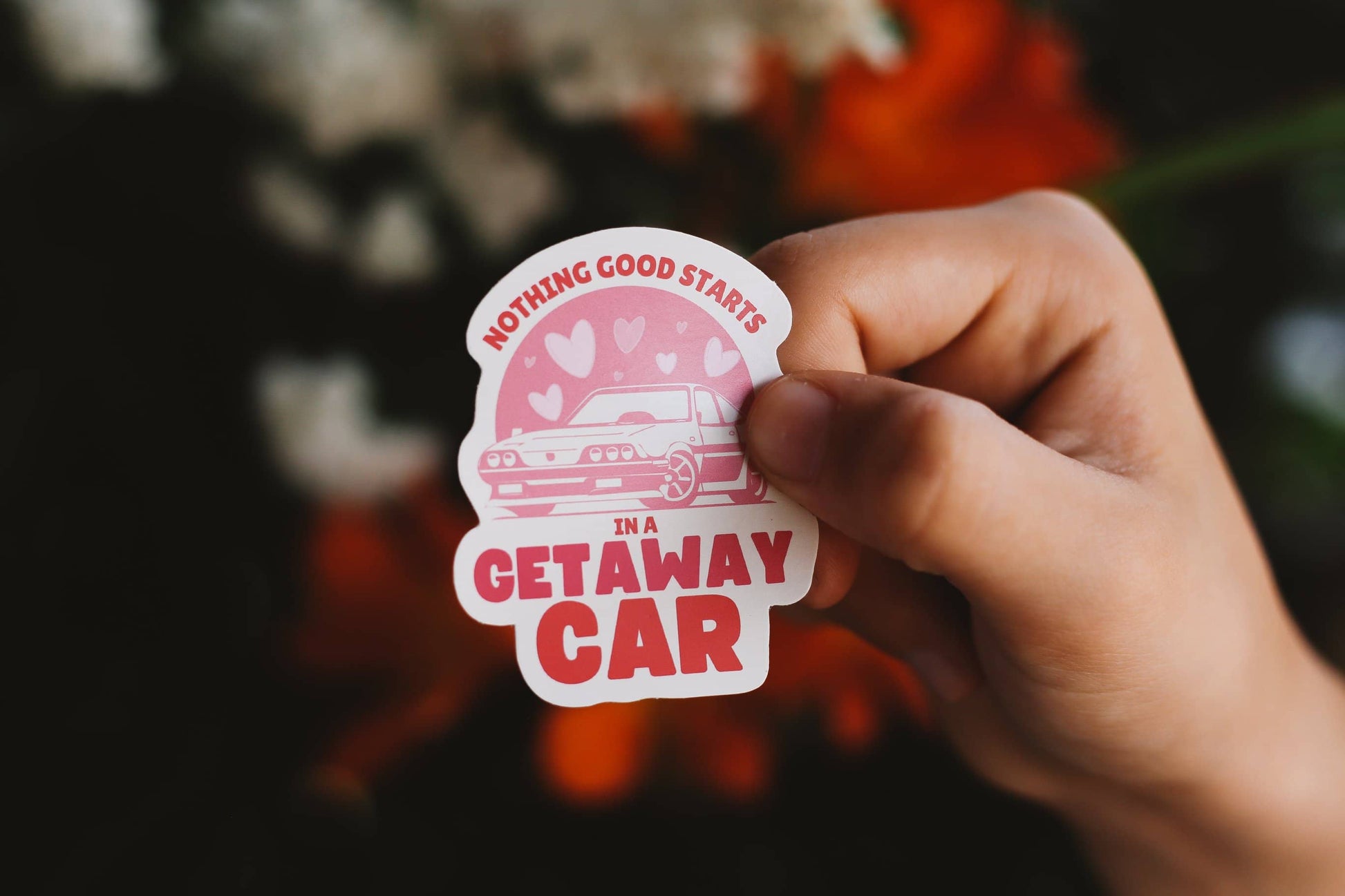 Hand holding a sticker with text 'Nothing good starts in a getaway car' against a blurred background