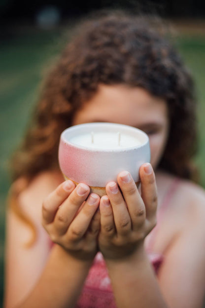 A child holding one of Àine & Co.'s Comfort Candle cups in Flós (pale pink).