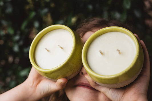 Child holding Àine & Co. ceramic Comfort Candle Cup in Sásta, featuring a yellow glaze and two cotton wicks.