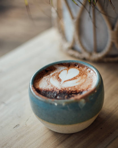 Àine & Co. Comfort Cup in Murúch (Mermaid). A reusable ceramic candle cup featuring a light teal colour, filled with a cappuccino.