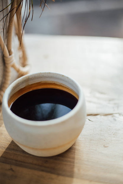 Àine & Co. Comfort Cup in Gealghrá (Tender Pure Love). A reusable ceramic candle cup featuring a speckled white colour, filled with black coffee.