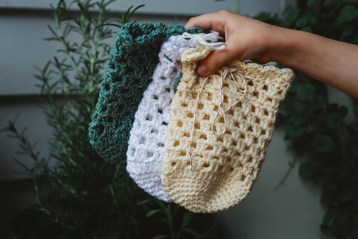 Hand holding Àine & Co hand crotchet gift sack in white, yellow and green