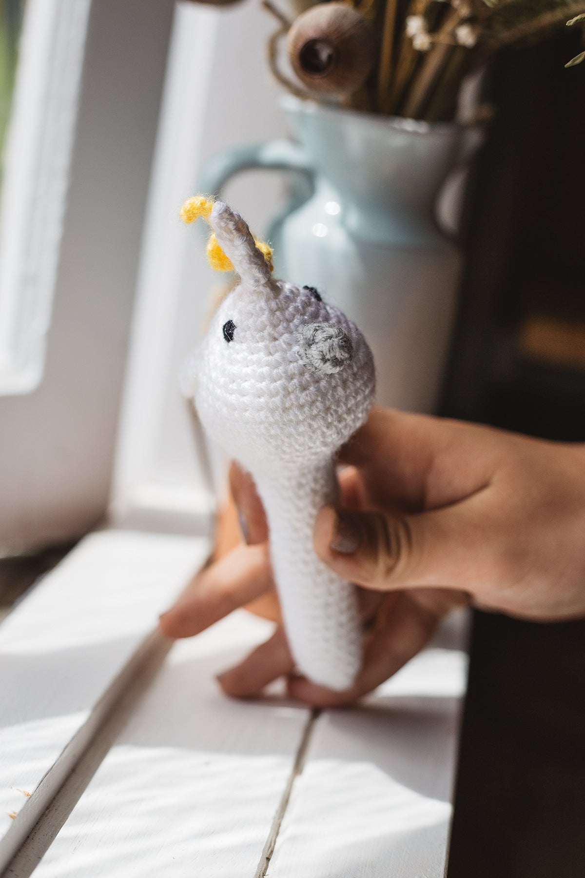Àine & Co. Crochet Baby Rattle in "Cockatoo", featuring white, yellow and grey cockatoo design