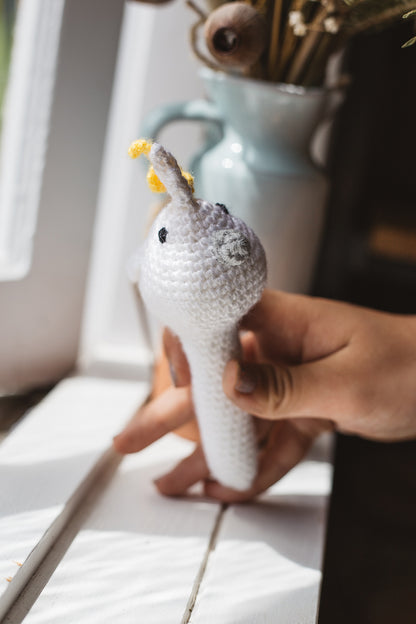 Àine & Co. Crochet Baby Rattle in "Cockatoo", featuring white, yellow and grey cockatoo design