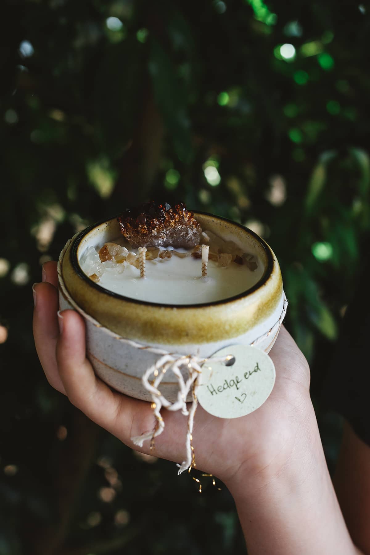 Hand holding Àine & Co. Crystal Comfort Candle in Hedge End, featuring ceramic white and yellow glazed mug, with citrine crystal atop the candle wax