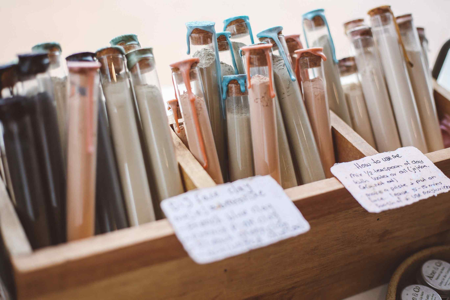 A wooden display box filled with many small glass tubes or vials containing different colored substances, with handwritten notes attached to the front.