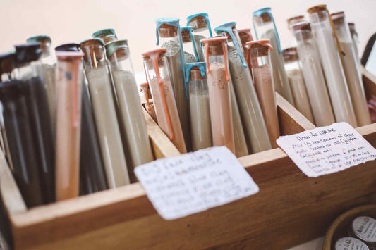 A wooden display box filled with many small glass tubes or vials containing different colored substances, with handwritten notes attached to the front.