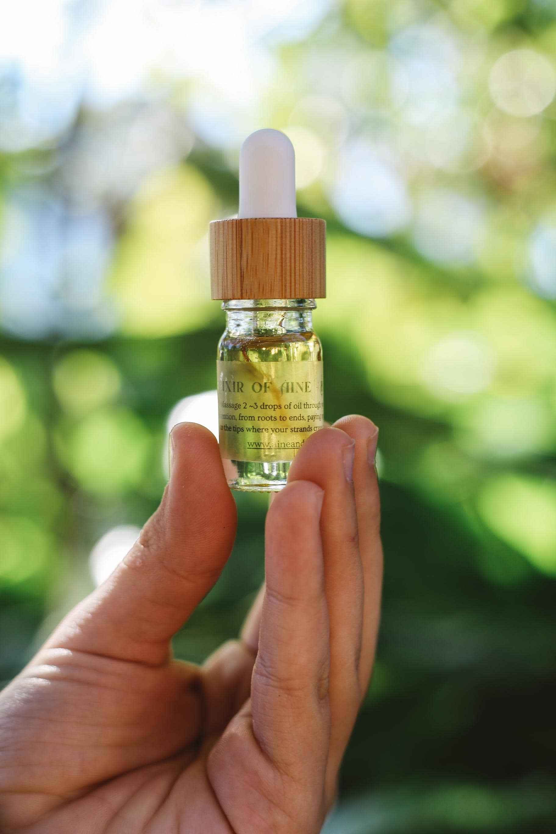 Hand holding a dropper bottle with a green liquid against a blurred natural background