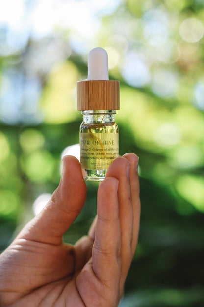 Hand holding a dropper bottle with a green liquid against a blurred natural background